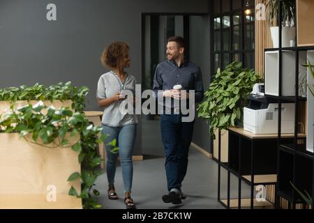 Diverse employees walking in office, chatting, discussing project Stock Photo