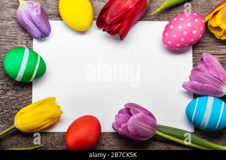 Hand-painted easter eggs with tulips on blank greeting card over wooden background copy space for text Stock Photo