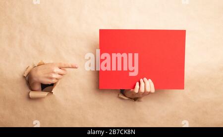 Lady pointing at empty red sheet through gap in kraft paper, blank space for design Stock Photo