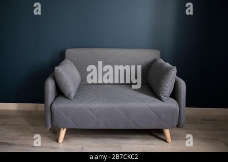 Gray soft sofa with 2 pillows. Modern design sofa on blue background in empty room. Copy space. Stock Photo