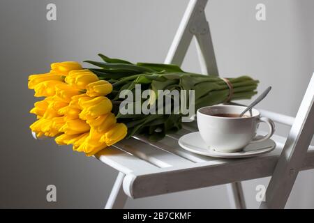 A bouquet of yellow tulips wrapped in white craft paper lies on a chair Stock Photo