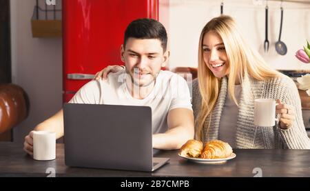 Family of two having breakfast while using laptop in kitchen, panorama Stock Photo