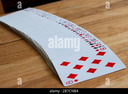 Spread of playing cards with the eight of diamonds standing out, wooden surface, background, gambling, magic Stock Photo