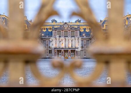 The East facade of the Palace of Versailles seen through the gilded bars of the entrance gate, France Stock Photo