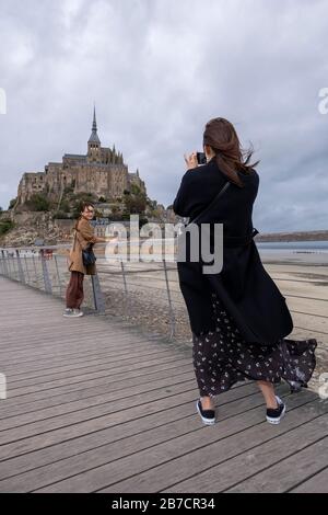 Asian tourist taking pictures of a friend in front of the Mont Saint-Michel, Normandy, France, Europe Stock Photo