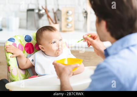 Hungry baby eating healthy kid food in kitchen Stock Photo