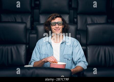 Handsome young man with popcorn and 3D glasses in cinema Stock Photo