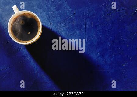 Coffee cup on blue background, top view. Morning shadow from a cup on a concrete table. Stylish design. Copyspace. Stock Photo
