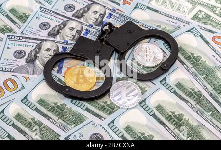 Steel police handcuffs and coins of cryptocurrency lying on the banknotes of american dollars Stock Photo