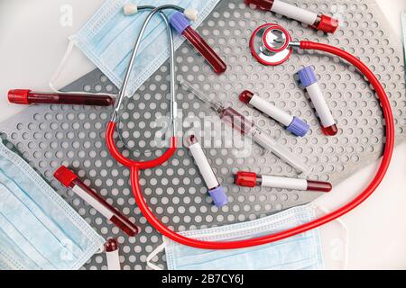 Blood sample along with syringe, protective mask and stethoscope on metal surface Stock Photo
