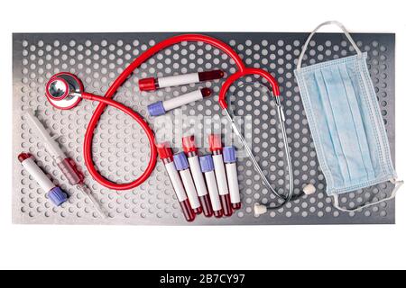 Flat lay of blood sample along with syringe, protective mask and stethoscope on metal surface Stock Photo