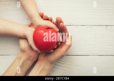 red heart in child and mother hands on white wooden background. concept of love, charity, empathy Stock Photo