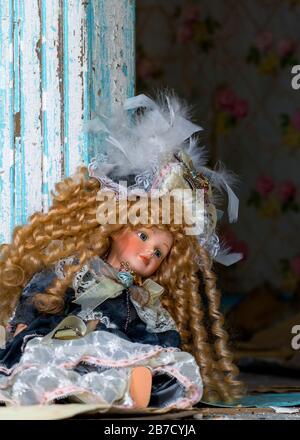 An old doll sitting against the door frame in an abandoned house. Debris litters the floor, paint is peeling from the frame. Portrait orientation. Stock Photo