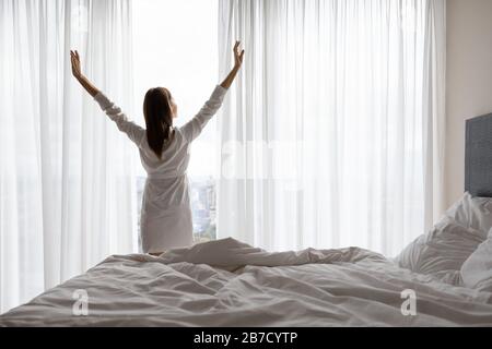Young woman in night gown stretching muscles near window. Stock Photo
