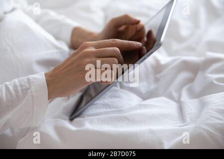 Young woman lying in bed, using computer digital tablet. Stock Photo