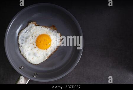 Fried organic egg sunny side up seasoned with salt and pepper in a frying pan with copy space. Stock Photo