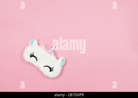 White fluffy fur sleep mask unicorn with closed eyes and small ears on pastel pink paper background, copy space. Top view, flat lay. Concept of vivid Stock Photo