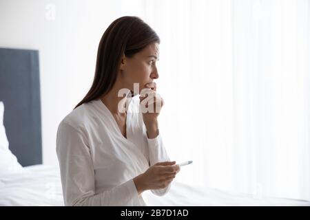 Thoughtful young woman holding quick plastic pregnancy test in hands. Stock Photo