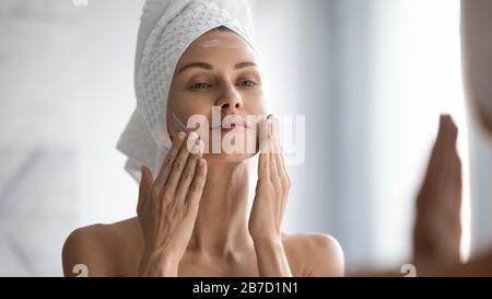 Smiling young pretty lady wrapped in towel smoothing perfecting skin. Stock Photo