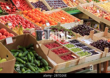 Fresh fruits, berries and vegetables are in trays in the market. Cucumbers, raspberries, cherries, gooseberries, tomatoes and other fruits lie in rows Stock Photo
