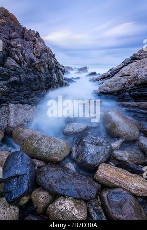A seascape photograph taken after sunset on a windy evening, with misty waves crashing on the rocks by the South Coast in South Africa Stock Photo