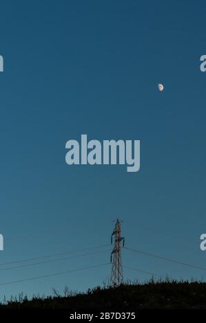 Electric pole in a mountain with the moon in the background in blue sky Stock Photo