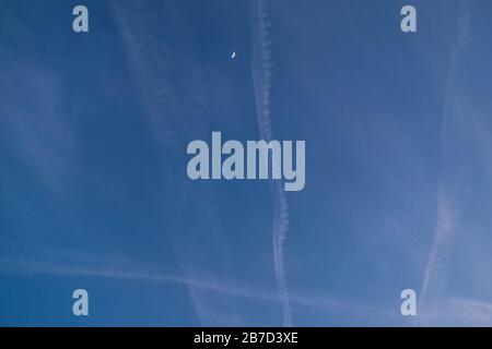 Crossing of airplane trails with crescent moon in blue sky Stock Photo