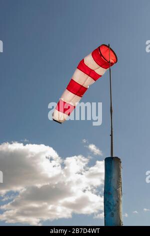 A windsock on flagpole against blue cloudy sky white and red striped conical textile tube Stock Photo