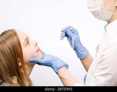 Pediatrician or doctor taking nasal mucus test sample from elementary age girl's nose performing respiratory virus testing procedure Stock Photo