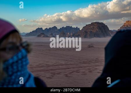 WADI RUM, JORDAN - JANUARY 31, 2020: Blurred silhouettes of tourists waiting for sunset on the red sand. Winter puffy clouds windy afternoon sky, beautiful desert, Hashemite Kingdom of Jordan Stock Photo