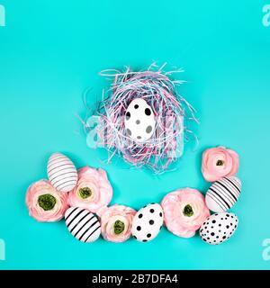 Decorative bird nest with creative graphic eggs and ranunculus flowers on blue pastel background. Easter concept. Stock Photo