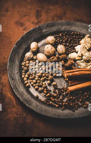 Turkish traditional seven spice Yedi Bahar mix for cooking. Black pepper, ginger, cloves, nutmeg, cinnamon, allspice and alpinia root in black plate o Stock Photo