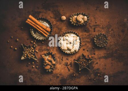 Turkish seven spice Yedi Bahar mix. Flat-lay of black pepper, ginger, cloves, nutmeg, cinnamon, allspice and alpinia root in tin cookie molds over rus Stock Photo