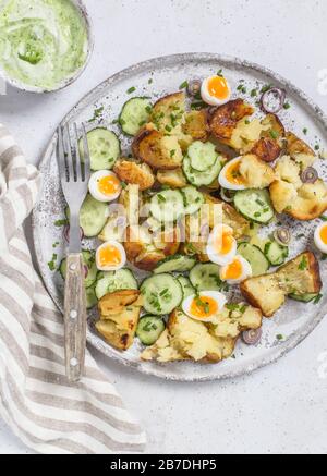 Roasted potato, cucumber and quail eggs salad, served on grey plate with green dressing on the side. Stock Photo
