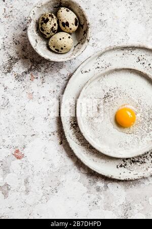 Cracked quail egg on a grey ceramic plates, few eggs in a small grey bowl, grey background. Stock Photo