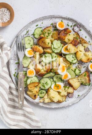 Roasted potato, cucumber and quail eggs salad, served on grey plate, served with salt in wooden bowl. Stock Photo