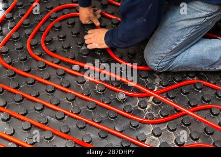 Worker who instal tubes of radiant underfloor heating installation Stock Photo