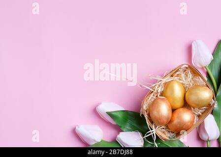 Congratulation Happy Easter card from handmade painted chicken and quail eggs, tulips flowers on a pink background, copy space. Top view. Stock Photo