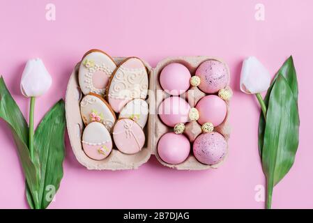 Happy Easter congratulation card from handmade painted pink chicken eggs, two tulips flowers and homemade baked cookies on a pink background, copy spa Stock Photo