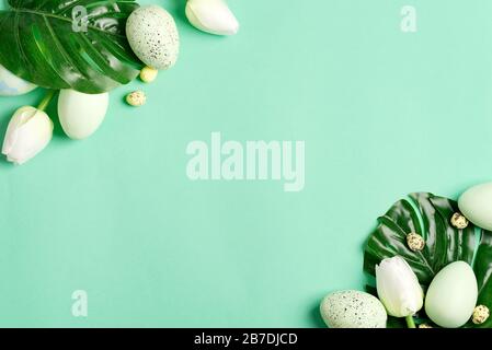 Easter festive card from fresh green tropical leaf of Monstera plant, green eggs and small quail eggs on a light turquoise background, copy cpace. Hap Stock Photo