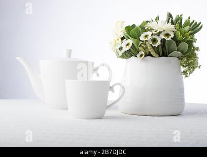 Light gray gradient background with contemporary white tea set and fresh flowers in a white pottery vase Stock Photo