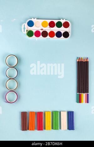 Art collection from watercolor paints, paper ribbons, colorful pensils and plasticine on a pastel blue background with copy space. Flat lay Stock Photo