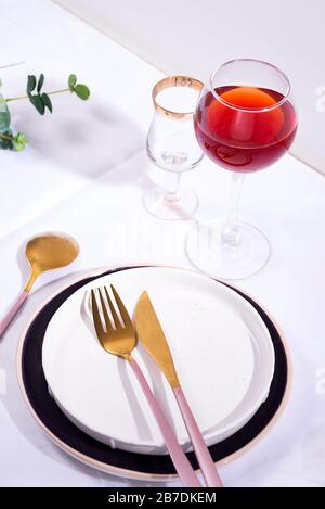 Tableware and decorations for serving a festive table. Plates, red wine glass and cutlery on white textile background. Stock Photo