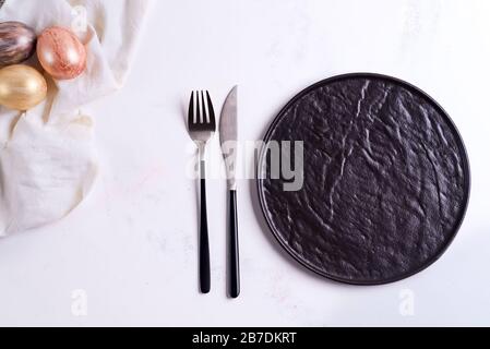 Easter table setting from above. Stone black empty plate, cutlery, napkin and golden eggs on stone Stock Photo