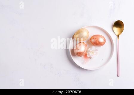 Happy Easter card with handmade painted eggs on a ceramic plate and golden spoon on a light grey marble background, copy space. Easter concept. Stock Photo