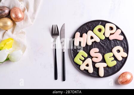 Easter table setting with tulip flowers, golden eggs and cookie on plate. Top view over white marble table , Stock Photo