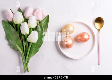 Easter plate with spring tulips and spoon and golden eggs on stone Stock Photo