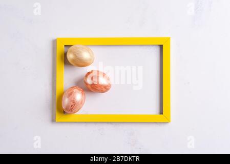 Easter greeting card and golden eggs in the yellow photo frame on a marble background Stock Photo