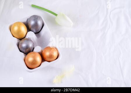Golden Easter Eggs in ceramic egg tray with tulip on white table. Easter background or easter concept. Stock Photo