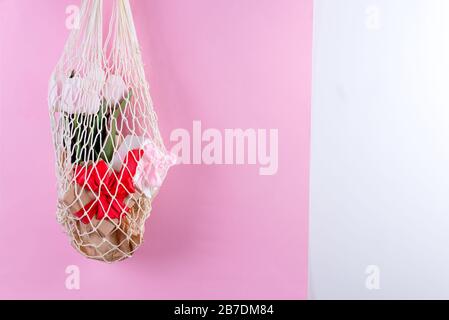 Reusable shopping bags with paper gift boxes and fresh spring tulips flowers in woman's hand against a pink background. Stock Photo